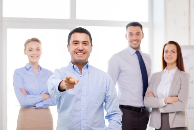 Foto conceito de negócios e escritório - empresário bonito sorridente com equipe no escritório apontando o dedo para você