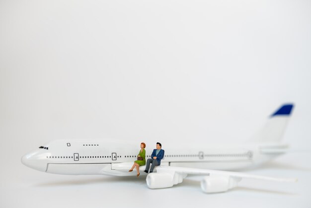 Conceito de negócios e viagens. figura em miniatura de empresário e empresária pessoas sentadas na asa do modelo do mini avião