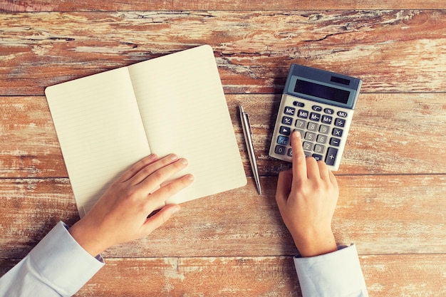 conceito de negócios, educação, pessoas e tecnologia - close-up de mãos femininas com calculadora, caneta e caderno na mesa