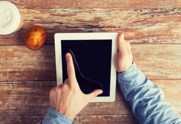 conceito de negócios, educação, pessoas e tecnologia - close-up de mãos masculinas com computador tablet pc, muffin e xícara de café na mesa