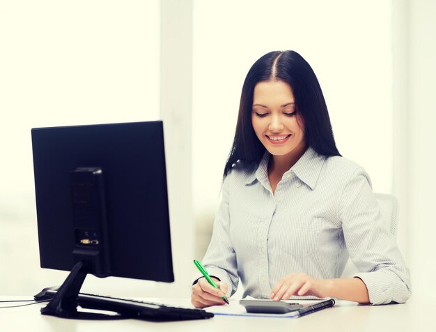 conceito de negócios, educação, tecnologia e impostos - sorridente mulher de negócios ou estudante com coputer, calculadora, caderno e caneta