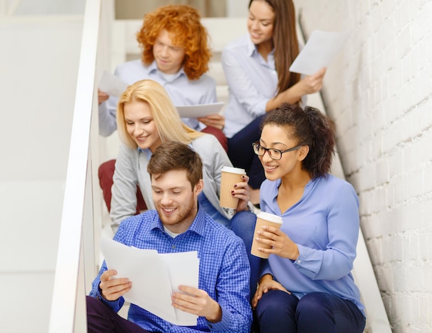 Foto conceito de negócios, escritório e inicialização - equipe criativa sorridente com papéis e café na escada