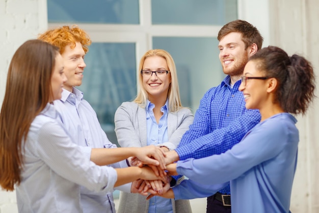 Foto conceito de negócios, escritório, gesto e inicialização - equipe criativa sorridente com as mãos umas sobre as outras sentadas no escritório