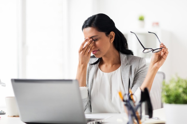 conceito de negócios, excesso de trabalho, prazo, visão e pessoas - empresária cansada de óculos, trabalhando no escritório e esfregando os olhos