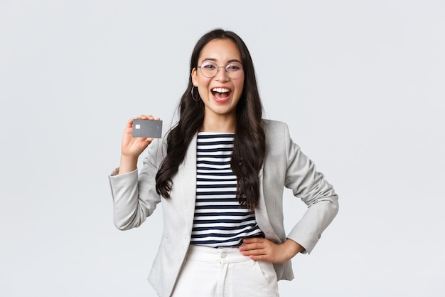 Conceito de negócios, finanças e emprego, empresário e dinheiro. rindo, alegre e extrovertida, gerente de escritório feminino, de terno branco e óculos, mostrando o cartão de crédito