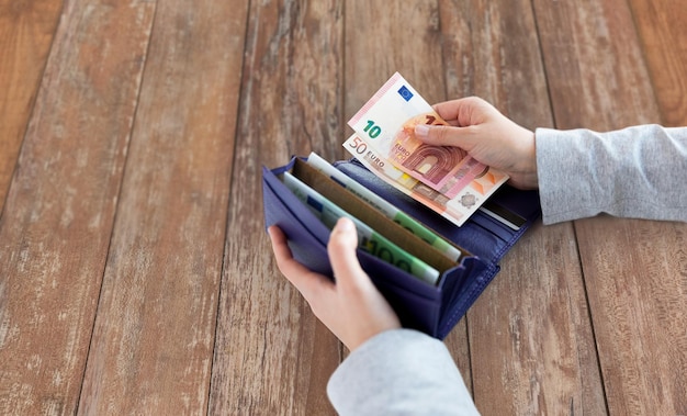conceito de negócios, finanças, economia, bancário e pessoas - close-up de mãos de mulher com carteira e dinheiro euro na mesa de madeira