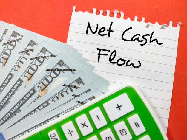 Conceito de negócios Fluxo de caixa líquido escrito em papel para cartas com dinheiro falso e calculadora em fundo vermelho