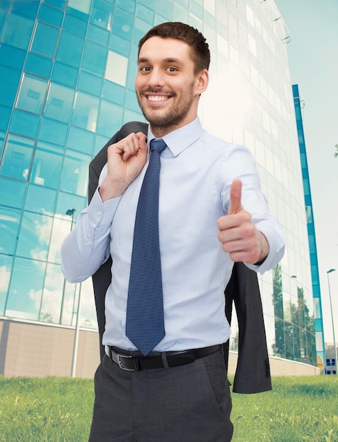 Foto conceito de negócios, gestos e pessoas - empresário jovem e bonito sorridente, mostrando os polegares sobre o fundo do centro de negócios