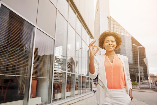 conceito de negócios, gestos e pessoas - jovem empresária afro-americana sorridente na cidade mostrando sinal de mão ok