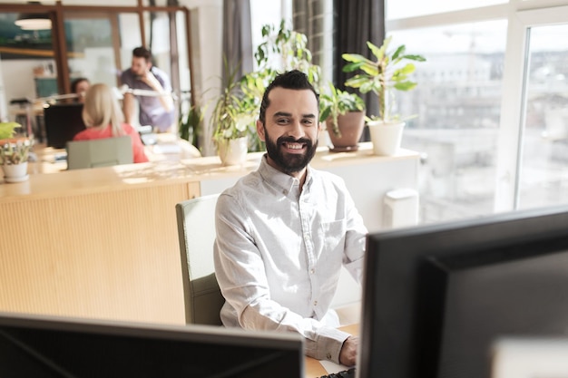 Conceito de negócios, inicialização e pessoas - empresário feliz ou trabalhador de escritório masculino criativo com computador