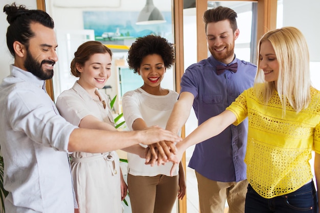 Foto conceito de negócios, inicialização, gesto, pessoas e trabalho em equipe - equipe criativa feliz com as mãos umas sobre as outras no escritório