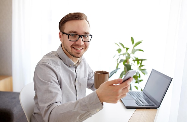 conceito de negócios, inicialização, tecnologia e pessoas - empresário feliz ou trabalhador masculino criativo enviando mensagens de texto no smarphone e tomando café no escritório doméstico