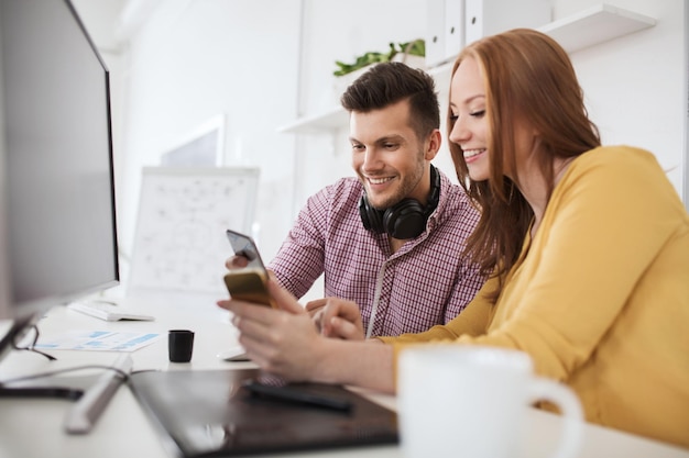 conceito de negócios, inicialização, tecnologia e pessoas - equipe criativa feliz com smartphones, computador e caneta tablet no escritório