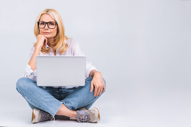 Conceito de negócios. Linda mulher madura sênior com um laptop sentado no chão em pose de lótus com uma expressão de cansaço e tédio.