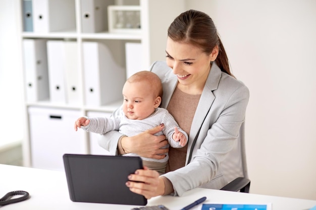 conceito de negócios, maternidade, multitarefa, família e pessoas - empresária sorridente feliz com bebê e tablet pc trabalhando no escritório