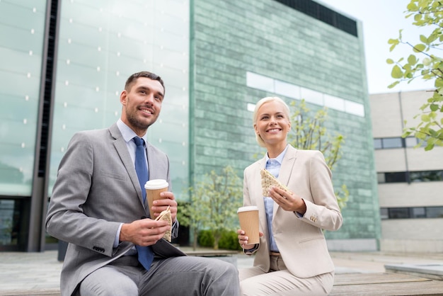 conceito de negócios, parceria, comida, bebidas e pessoas - empresários sorridentes com copos de papel em cima do prédio de escritórios