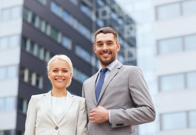 conceito de negócios, parceria, sucesso e pessoas - empresário sorridente e empresária em pé sobre prédio de escritórios