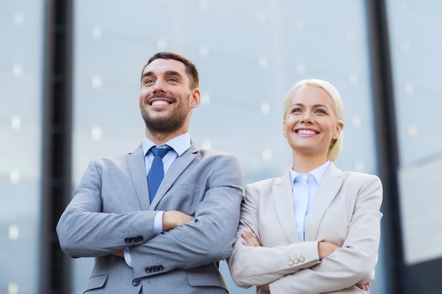 conceito de negócios, parceria, sucesso e pessoas - empresário sorridente e empresária em pé sobre prédio de escritórios