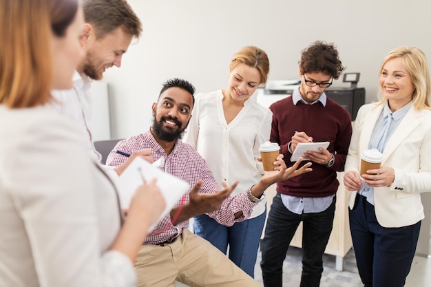 conceito de negócios, pausa, comunicação e pessoas - equipe criativa feliz com notebooks tomando café e conversando no escritório