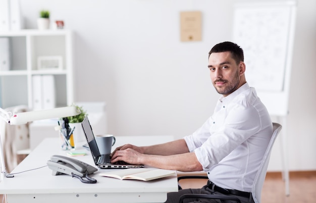 conceito de negócios, pessoas e tecnologia - empresário feliz com computador portátil no escritório