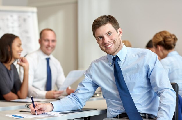 Conceito de negócios, pessoas e trabalho em equipe - empresário sorridente com grupo de empresários reunidos no escritório