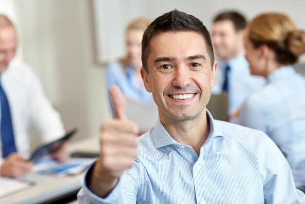 Foto conceito de negócios, pessoas, gestos e trabalho em equipe - empresário sorridente mostrando polegares para cima com grupo de empresários reunidos no escritório