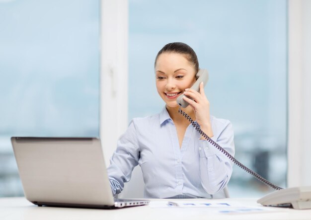 conceito de negócios, tecnologia e comunicação - empresária sorridente com telefone, laptop e arquivos no escritório