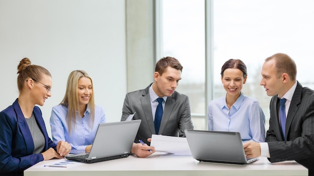 Conceito de negócios, tecnologia e escritório - equipe de negócios sorridente com laptops e documentos discutindo no escritório