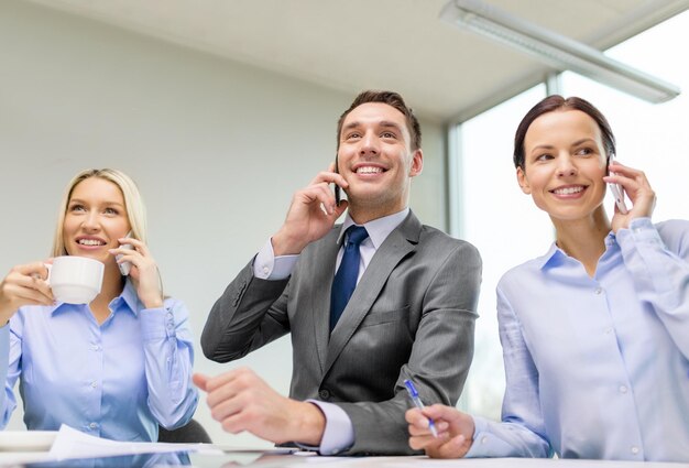 Conceito de negócios, tecnologia e escritório - equipe de negócios sorridente com smartphones fazendo chamadas no escritório