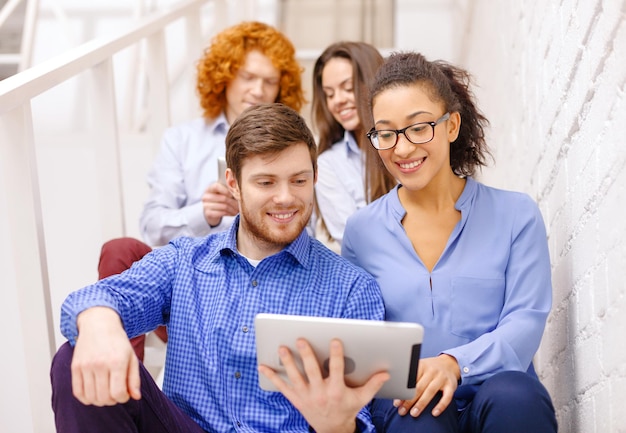 Foto conceito de negócios, tecnologia e inicialização - equipe criativa sorridente com computador tablet pc sentado na escada