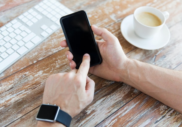 conceito de negócios, tecnologia e pessoas - close-up da mão masculina segurando o telefone inteligente e usando relógio com café e teclado na mesa de madeira