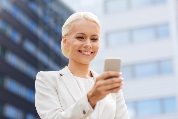 Conceito de negócios, tecnologia e pessoas - empresária sorridente com smartphone em prédio de escritórios