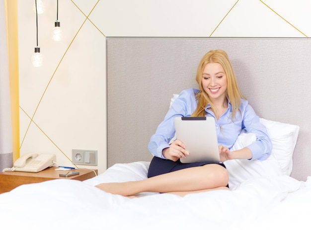 conceito de negócios, tecnologia, internet e hotel - empresária feliz com computador tablet pc deitado no hotel na cama