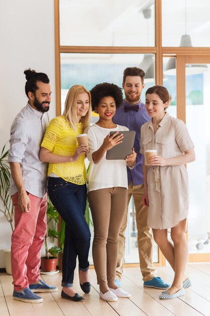 conceito de negócios, tecnologia, pessoas e trabalho em equipe - feliz equipe criativa internacional de duas mulheres e um homem com computador tablet pc e café no escritório