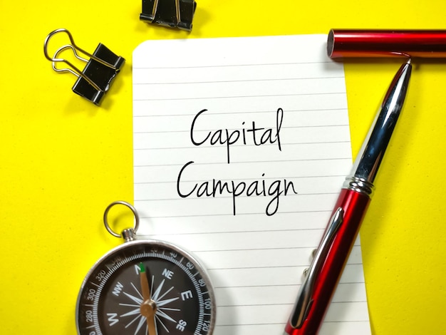 Conceito de negóciosTexto Capital Campaign escrevendo em papel timbrado com clipes de caneta e bússola em fundo amarelo