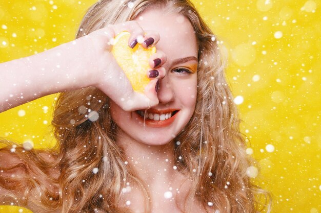 Conceito de neve, inverno, natal, emoções, saúde, pessoas, comida e beleza - garota modelo de beleza leva laranjas suculentas. Linda menina adolescente alegre com sardas. maquiagem amarela. sobre fundo de neve