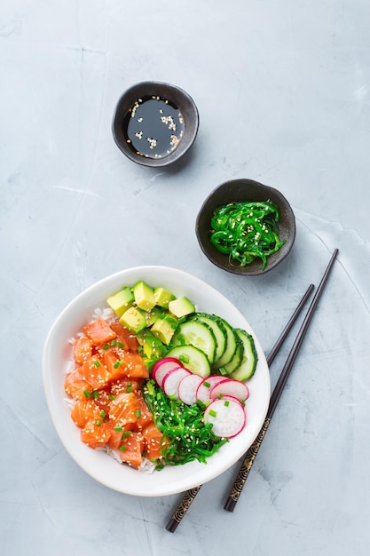 Conceito de nutrição de almoço de comida rápida e saudável tigela de puxão de salmão havaiano orgânico fresco com arroz de algas marinhas abacate pepino em uma mesa de cozinha moderna vista superior plana de fundo