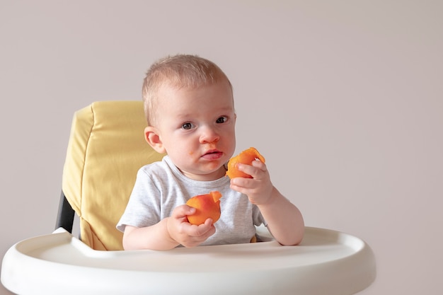 Conceito de nutrição de comida de bebê bebê sentado à mesa com damascos nas mãos