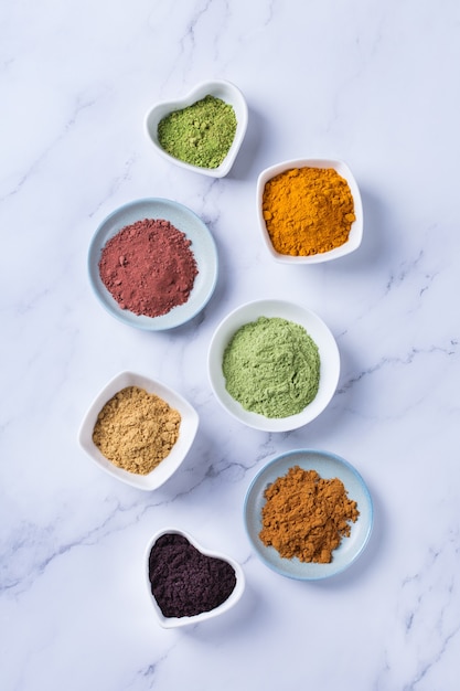 Conceito de nutrição equilibrada para uma dieta desintoxicante de antioxidantes de alimentação limpa. Variedade de pó de superalimento - açaí, açafrão, trigo, gengibre, canela, matcha. Fundo plano de mármore