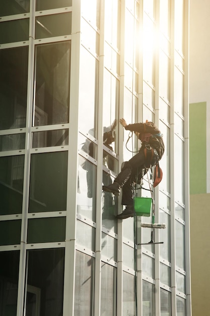 Conceito de obras urbanas industriais Trabalhador de montanhismo industrial de uniforme paira sobre edifício de fachada residencial