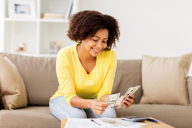 conceito de orçamento, finanças e pessoas - mulher afro-americana feliz com papéis e calculadora contando dinheiro em casa