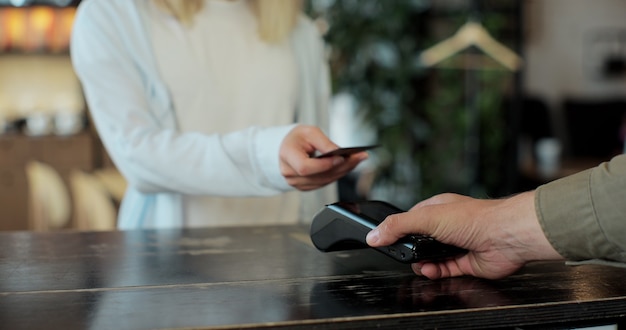 Conceito de pagamento móvel - close-up de jovem paga usando pagamento sem contato de cartão de crédito por seu pedido de café no café. O cliente usa o celular para pagar pelo terminal do banco.