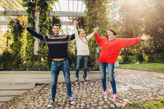 Conceito de pais e filhos família feliz se diverte ao ar livre, brincar feminino e masculino com criança balançando-a nas mãos fazer gestos ter um relacionamento maravilhoso desfrutar do ar fresco do outono