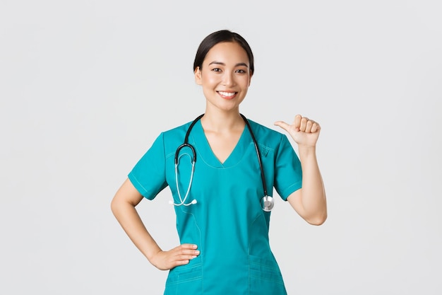 Conceito de pandemia de trabalhadores de saúde Covid19 Enfermeira médica asiática confiante profissional em uniforme apontando para si mesma e sorrindo garante que ela sabe o que faz fundo branco