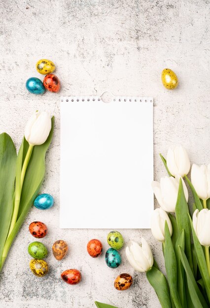 Conceito de páscoa e primavera. vista superior de tulipas brancas, calendário em branco e ovos de páscoa coloridos em fundo de concreto com espaço de cópia