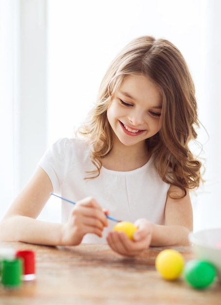 Conceito de páscoa, férias e criança - menina sorridente colorindo ovos para a páscoa