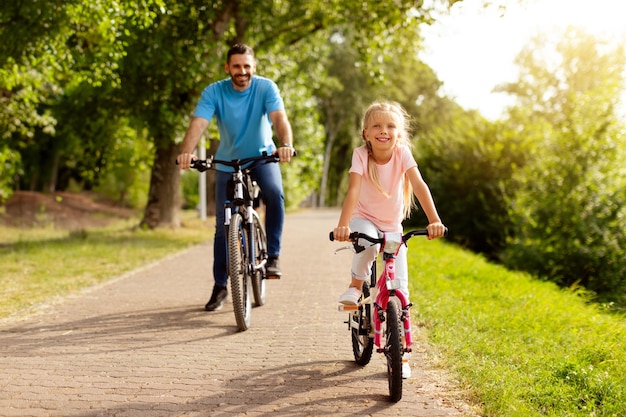 Conceito de passatempo familiar feliz pai de meia-idade e sua linda filha andando de bicicleta juntos em