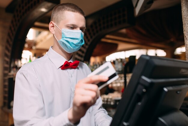 Conceito de pequenas empresas, pessoas e serviços. homem ou garçom na máscara médica no balcão com caixa trabalhando no bar ou cafeteria.