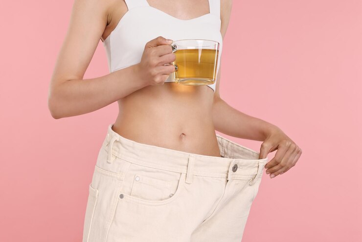 Foto conceito de perda de peso mulher com xícara de chá dietético e calças grandes em fundo rosa em close-up