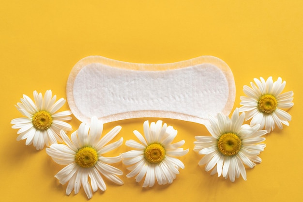 Conceito de período de menstruação Almofada feminina branca higiênica com flores de camomila em fundo amarelo Proteção da menstruação Saúde da mulher